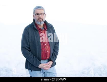 Mann, 56 Jahre, graues Haar und Bart, im Winter draußen stehend mit Schnee im Hintergrund, Stockfoto
