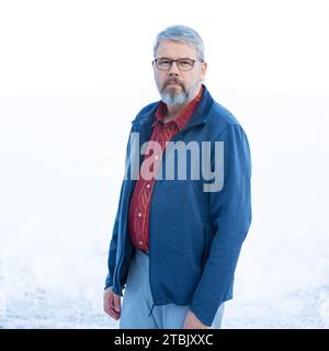 Mann, 56 Jahre, graues Haar und Bart, im Winter draußen stehend mit Schnee im Hintergrund, Stockfoto