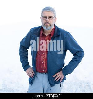 Mann, 56 Jahre, graues Haar und Bart, im Winter draußen stehend mit Schnee im Hintergrund, Stockfoto