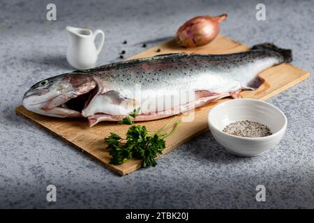 Ein frisch gefangener Fisch wird auf einem Schneidebrett mit verschiedenen aromatischen Gewürzen und einer frischen Zwiebel um den Fisch gelegt Stockfoto