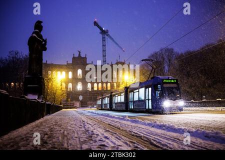 München, Deutschland. Dezember 2023. Vor dem Maximilianeum, Sitz des Bayerischen Landtags, fallen dicke Schneeflocken vom Himmel, während im Vordergrund eine Straßenbahn die Maximilianbrücke überquert. Die Statue von Pallas Athena ist links zu sehen. Quelle: Matthias Balk/dpa/Alamy Live News Stockfoto