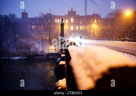 München, Deutschland. Dezember 2023. Vor dem Maximilianeum, Sitz des Bayerischen Landtags, fallen dicke Schneeflocken vom Himmel, während ein Radfahrer im Vordergrund über die Maximilianbrücke fährt. Die Statue von Pallas Athena ist links zu sehen. Quelle: Matthias Balk/dpa/Alamy Live News Stockfoto