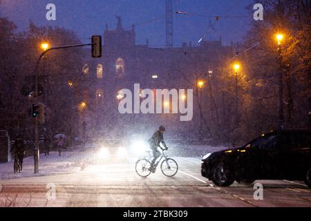 München, Deutschland. Dezember 2023. Vor dem Maximilianeum, Sitz des Bayerischen Landtags, fallen dicke Schneeflocken vom Himmel, während ein Fahrrad im Vordergrund die Straße überquert. Quelle: Matthias Balk/dpa/Alamy Live News Stockfoto