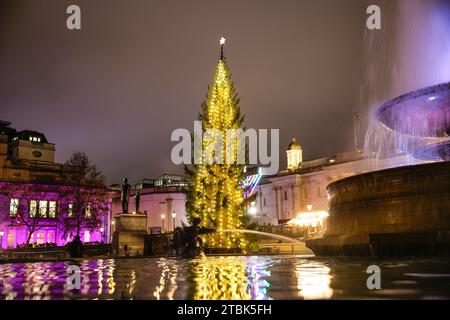 London, Großbritannien. Dezember 2023. Der beleuchtete Baum mit den Springbrunnen und Menora im Hintergrund. Die jährliche Zeremonie zum Einschalten des Weihnachtsbaums am Trafalgar Square sorgt für eine festliche Atmosphäre im Zentrum Londons, darunter Weihnachtslieder und Chorgesang. Jeden Dezember schickte ein Baum von Norwegen nach London als Geschenk, um Großbritannien für seine Unterstützung während des Zweiten Weltkriegs zu danken. Quelle: Imageplotter/Alamy Live News Stockfoto