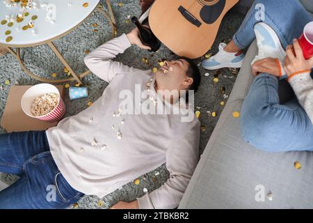 Betrunkener junger Mann, der nach der Neujahrsfeier zu Hause auf dem Boden schläft, Blick von oben Stockfoto