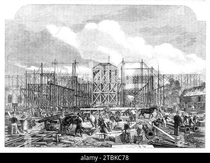 Fortschritt des Gebäudes für die Internationale Ausstellung von 1862, (1861). "...die Form des Gebäudes scheint in seinen realen Proportionen, den Backsteinmauern, als unser Künstler den Ort besuchte, der sich auf etwa 30 Fuß erhob. Vom Boden aus... werden die Reihen von eisernen Säulen, die den Boden bestreuen, schnell in die Struktur aufgenommen... die Gitterträger, die den Boden der Galerien stützen, dürften unter außergewöhnlichen Umständen ein Gewicht von 28 bis 30 Tonnen tragen. Einige von ihnen wurden getestet und zeigten ein Gewicht von 72 bis 76 bis Stockfoto