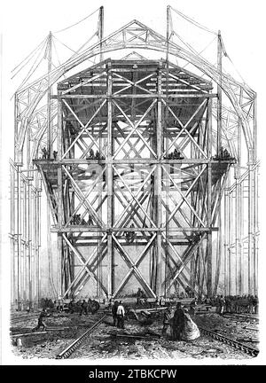 Fortschritt des großen Ausstellungsgebäudes: Die beim Bau des Kirchenschiffs verwendete Traversionsplattform, 1861. "...das erstaunlichste und umfangreichste der arbeitssparenden Arbeiten ist ein gigantisches Wandergerüst, das auf zwölf Rädern gebaut wurde und auf Schienen über die gesamte Länge des Mittelschiffs hinauf und hinunter läuft. Dieses riesige Gebäude ist 60 Fuß groß. Quadratisch und 100 ft. Hoch und wiegt fast 300 Tonnen. Aber... vier Männer mit Hebeln können es mit einer gewissen Geschwindigkeit auf jeden Teil der Werke bewegen. Sie wird zum Heben der oberen Säulen, der riesigen runden Holzrippen des verwendet Stockfoto