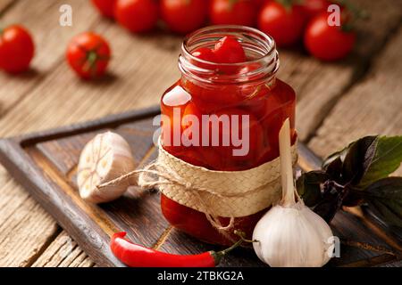 Konservierte Kirschtomaten in einem offenen Glas, Knoblauch, Chili-Paprika, frische Tomaten, Gewürze und Kräuter für Marinade auf hölzernem Hintergrund. Eingelegt Stockfoto