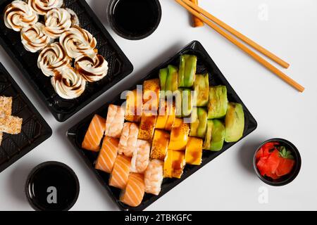 Ein Set von hellen mehrfarbigen Sushi-Rollen mit Garnelen, Lachs, Avocado in Plastikverpackung, chinesischen Essstäbchen, Soße, Ingwer auf weißem Hintergrund, Stockfoto