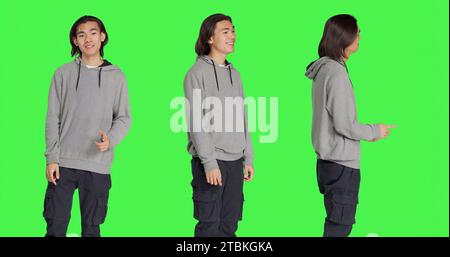 Asiatische Person zeigt ein Genehmigungszeichen über dem Hintergrund des Greenscreen, macht ja-Gesten und lächelt. Junger Mann mit optimistischem Gesichtsausdruck, der zufrieden ist und Zustimmung ausdrückt. Stockfoto