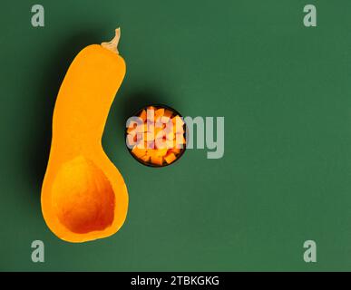 Die Hälfte eines orangen süßen Butternusskürbis und Kürbiswürfeln in einer Schüssel auf grünem Hintergrund, Draufsicht. Gesundes Gemüse, Vegetarismus. Stockfoto