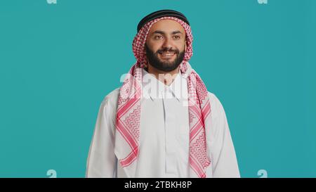 Die Person aus dem Nahen Osten gibt die Daumen vor der Kamera hoch und drückt ihre Zustimmung und Positivität aus, während sie traditionelle muslimische Kleidung trägt. Junger Erwachsener in natürlicher arabischer Kleidung, wie Zeichen. Stockfoto