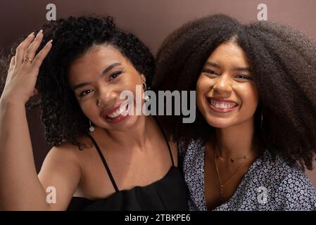 Halbgeschlossenes Porträt zweier glücklicher junger Freunde. Freundschaftskonzept. Isoliert auf lachsfarbenem Hintergrund. Stockfoto