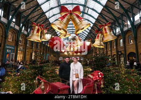 London, Großbritannien. Ein Paar posiert für ein Foto auf dem Apple Market von Covent Garden, der mit festlichen Riesenglocken und Kugeln dekoriert ist. Stockfoto