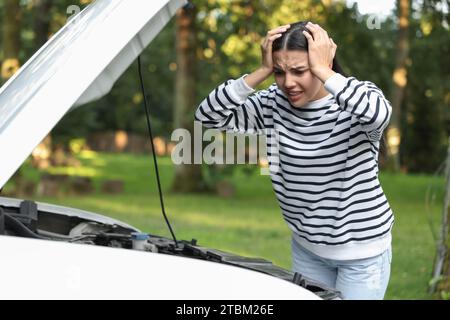 Gestresste junge Frau in der Nähe von gebrochenem Auto im Freien Stockfoto