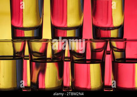 Eine Ansammlung kleiner, mit Wasser gefüllter Gläser, die in Schichten auf einem zweifarbigen Hintergrund angeordnet sind, verursacht Lichtbeugung Stockfoto