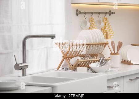 Waschbecken und Wäscheständer mit sauberem Geschirr und Besteck auf der Arbeitsplatte in der Küche Stockfoto