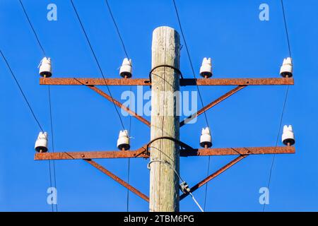 Alte Telefonstange mit Telefondrähten und weißen Porzellan-Isolatoren vor blauem Himmel, Schweden Stockfoto