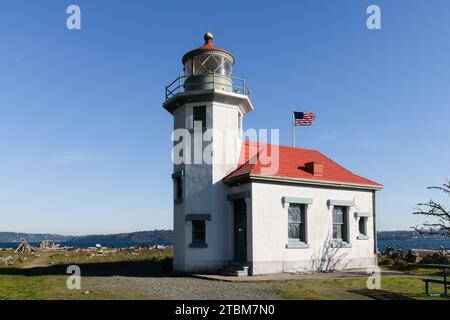 Maury Island, WA, USA - 30. Oktober 2023; Point Robinson Lighthouse am Puget Sound mit windiger amerikanischer Flagge und blauem Himmel Stockfoto