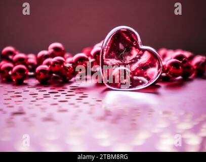 Glänzend transparent Herz und eine Gruppe von roten Perlen. Perfekte Valentinstag Grußkarte Hintergrund. Bild horizontal in rosa Ton Stockfoto