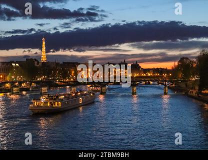 Frankreich, 03. April 2019. Wunderschönes NachtParis, glitzernder Eiffelturm, Brücke Pont des Arts über die seine und Touristenboote Stockfoto