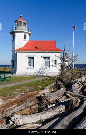 Maury Island, WA, USA - 30. Oktober 2023; Point Robinson Lighthouse mit Treibholz und amerikanischer Flagge im Wind Stockfoto