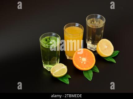 Drei Gläser mit verschiedenen Zitrussäften auf schwarzem Hintergrund, neben Reifen Früchten. Nahaufnahme. Stockfoto