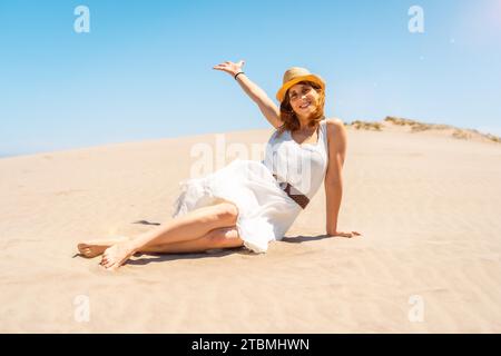 Glückliche Frau, die den Arm hebt, sitzt auf einer Düne am Meer in Cabo de Gata, Spanien Stockfoto