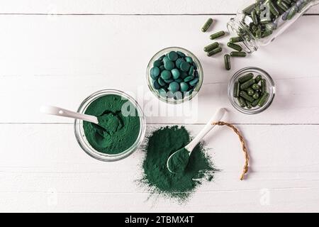 Runde blau-grüne natürliche Spirulina-Algentabletten und Pulver in Schüssel auf weißem Hintergrund. Medizinisches Gefäß mit Algenkapseln. Natürliche Nahrungsergänzungsmittel Stockfoto