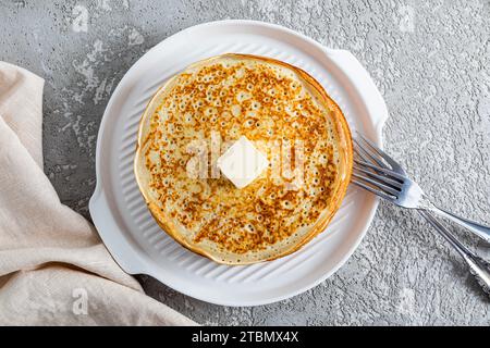 Köstliche frisch gebackene Pfannkuchen mit einem Klecks Butter auf einem runden Keramiktablett. Draufsicht. Grauer Zementhintergrund Stockfoto