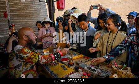 (231208) -- PEKING, 8. Dezember 2023 (Xinhua) -- Besucher kaufen antike „Visa“ an Li Sens Stand am Jiayu Pass in Jiayuguan City, nordwestchinesische Provinz Gansu, 14. Juli 2023. Li Sen, 43, verdient seinen Lebensunterhalt, indem er die Rolle eines alten „Generals“ in der malerischen Gegend des Jiayu-Passes in der Stadt Jiayuguan, der nordwestlichen chinesischen Provinz Gansu, spielt. Besucher können alte „Visa“ an seinem Stand kaufen. Diese Dokumente wurden von Li entworfen und bilden einen wesentlichen Teil des Rollenspiels, sodass Touristen zurück ins alte China reisen können. Mit Blick auf die Zukunft plant Li, den Hi systematisch zu organisieren Stockfoto