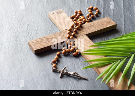 Holzkreuz, Rosenkranz und Palme auf schwarzem Marmorhintergrund, palmensonntag-Konzept Stockfoto