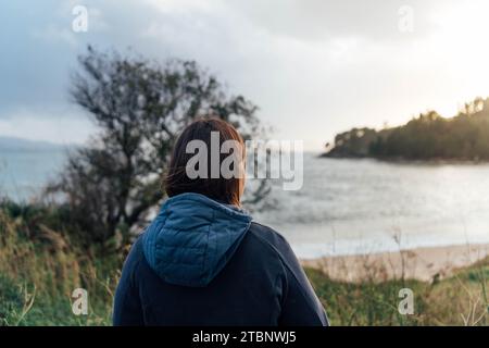 Eine junge Frau, die den Sonnenuntergang am Strand ansieht Stockfoto
