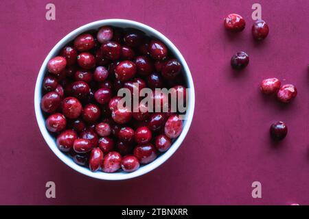 Überkopf-Schuss von Preiselbeeren in weißer Schüssel auf roter Oberfläche. Stockfoto