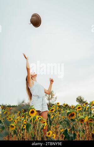 Ein junges Mädchen im Sommer, das einen Hut in die Luft wirft, umgeben von Blumen. Stockfoto