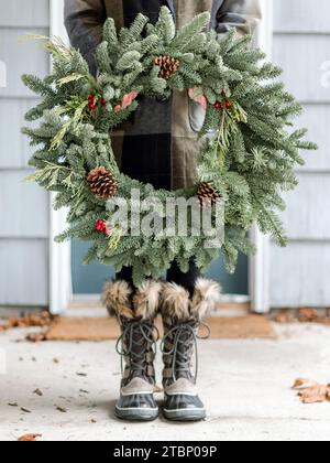 Stilvolle Frau mit Weihnachtskranz vor der Haustür Stockfoto