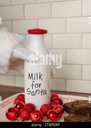 Der Weihnachtsmann greift nach einer Flasche Milch neben Brownies Stockfoto