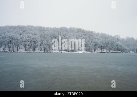 Tiefgraues Eis bedeckt See oder Fluss. Gefrorene Landschaft. Winterliche Waldbäume am Ufer Stockfoto