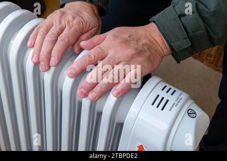 Nahaufnahme einer Person, die die Hände auf eine tragbare elektrische Heizung legt, um sie auch im Winter warm zu halten. Stockfoto