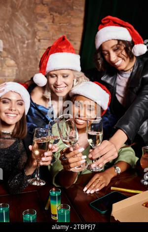 Unbeschwerte, multiethnische Freundinnen, die Champagner anklitzen, während sie Weihnachten in der Bar feiern Stockfoto