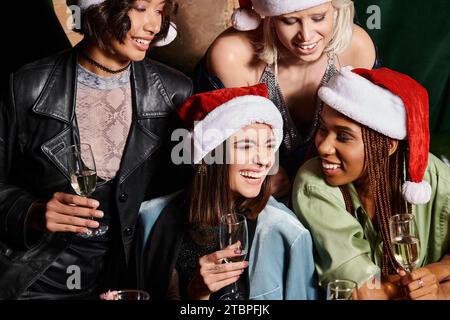 Unbeschwerte multikulturelle Freundinnen in Weihnachtshüten feiern Silvester mit Champagner in der Bar Stockfoto