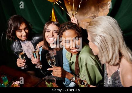 Überfreudige und elegante Frauen mit verschiedenen Rassen, die während der Geburtstagsfeier in der Bar Sektgläser halten Stockfoto