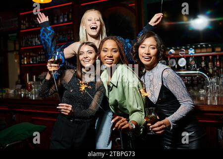 Fröhliche, multiethnische Freundinnen mit Cocktails und festlichen Funkeln, die Spaß in der Bar haben, festliche Party Stockfoto