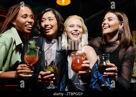 Glamouröse multiethnische Freundinnen mit köstlichen Cocktails, die lachen, während sie Spaß in der Bar haben Stockfoto