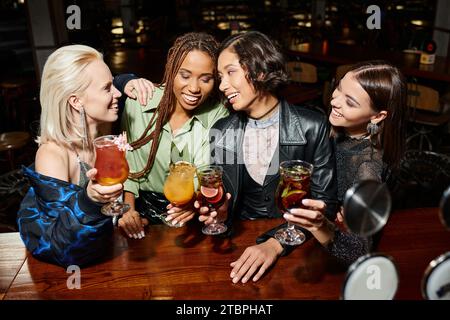 Verlockende und elegante, multiethnische Freundinnen, die mit Cocktails an der Bar und dem Nachtleben locken Stockfoto