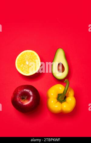 Gelber süßer Pfeffer, Apfel, Avocado und Zitrone vor rotem Hintergrund. Flache Lagen. Bio-Produkte und gesunde Lebensmittel Stockfoto