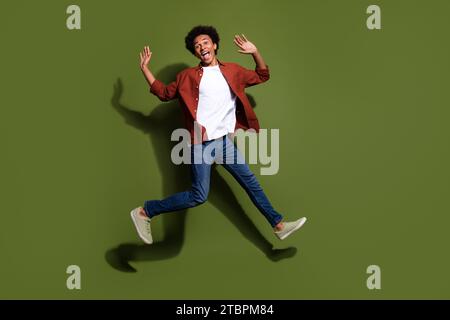 Foto in voller Länge des netten jungen Mannes, der rennend springt, haben Spaß gekleidetes stilvolles braunes Kleid isoliert auf khakifarbenem Hintergrund Stockfoto