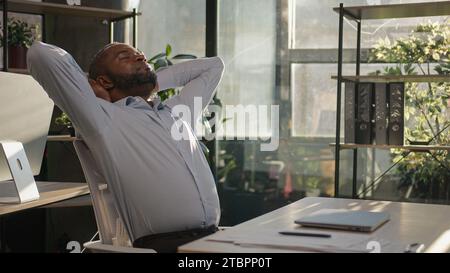 Entspannter, afroamerikanischer Geschäftsmann, Senior, glücklich, arbeiten Computer in der Nähe Laptop entspannen in sonnigen, warmen, bequemen Büro männlich Stockfoto