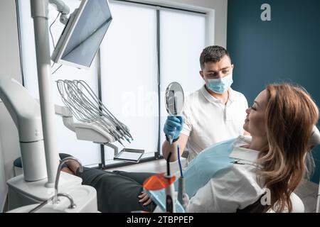 Der Arzt zeigt dem Patienten den Spiegel der Frau. Die Eingriffe in der Zahnklinik werden komfortabel und mit Liebe zum Detail durchgeführt Stockfoto