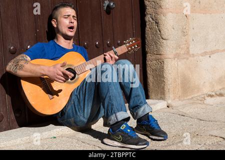 Straßenmusiker sitzt vor der Tür des Casa de los duques de Valencia und spielt Gitarre. Caceres, Extremadura, Spanien. Stockfoto